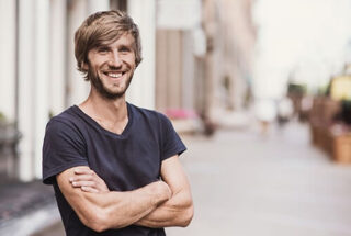 A man with his arms crossed smiles into the camera because he is glad he took advantage of the addiction treatment denver offers