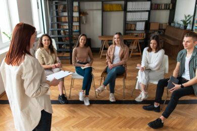 woman holding document talking to a seated group of persons