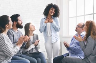 smiling woman standing up in front of clapping therapy circle peers at substance abuse treatment centers
